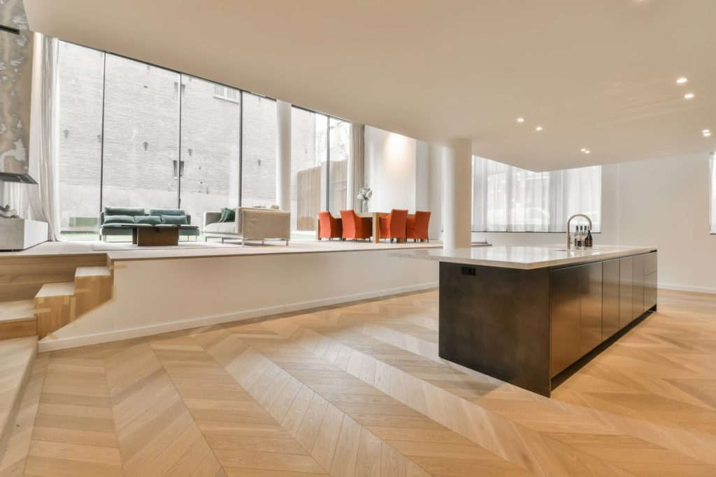 a modern kitchen with wood flooring and white walls in the room is very well lit by the large windows