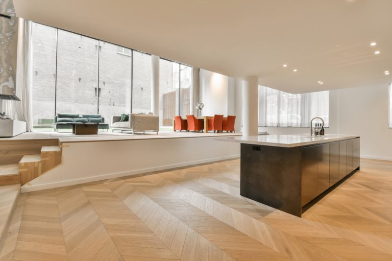 a modern kitchen with wood flooring and white walls in the room is very well lit by the large windows