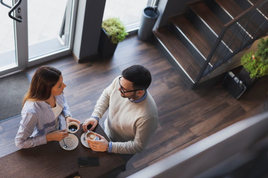 High angle view of a young couple in love on a date, standing next to a restaurant counter, drinking coffee and having a conversation