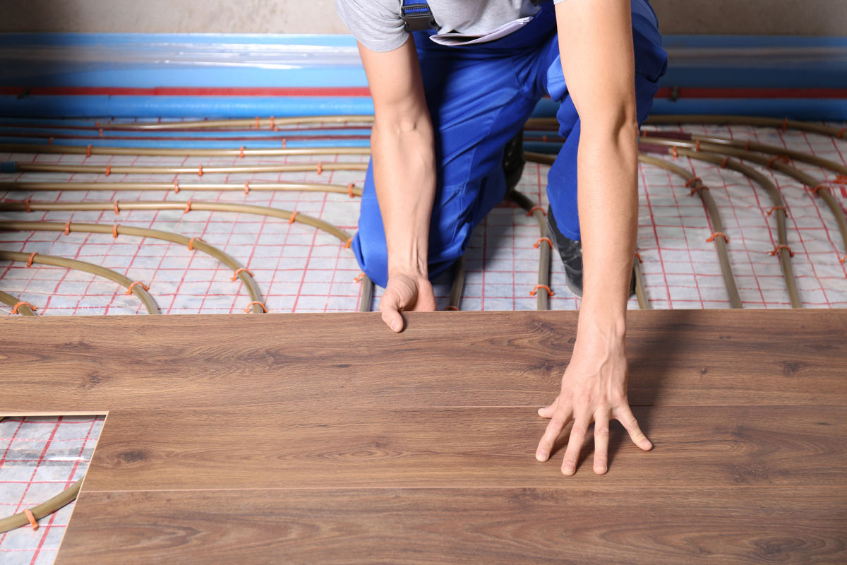 Worker installing new wooden laminate over underfloor heating system, closeup