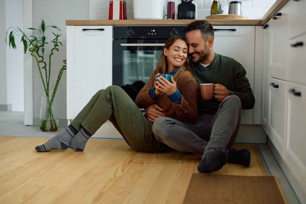 Affectionate couple sitting on the floor while enjoying in cup of tea at home. Copy space.